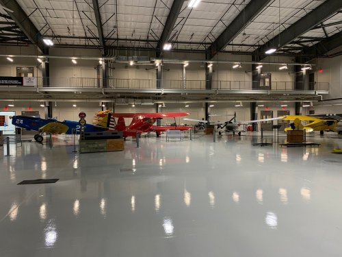 A spacious hangar displaying several vintage airplanes in various colors and designs, with polished floors and bright lighting.