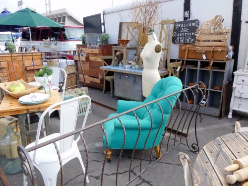 A vibrant turquoise chair among vintage furniture and decor items in an outdoor market setting.