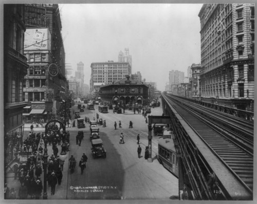 Historic black-and-white photo of a busy city intersection with streetcars, pedestrians, and buildings in the background.