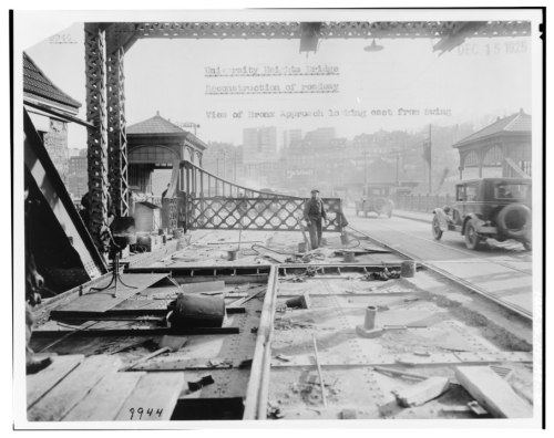Black and white photo of a bridge under reconstruction, with workers and vintage cars in the background.