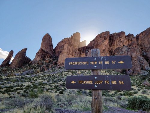 Signpost indicating trails: Prospector's View Trail No. 57 and Treasure Loop Trail No. 56, with rocky cliffs in the background.