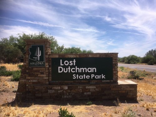 Sign for Lost Dutchman State Park in Arizona, surrounded by desert landscape and blue sky.