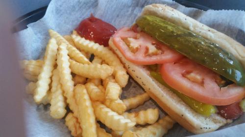 A hot dog topped with tomatoes and pickles, served with crinkle-cut fries and a side of ketchup.