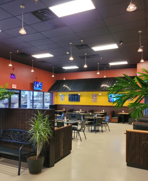 Interior of a restaurant featuring colorful walls, tables, chairs, and plants, with TVs mounted on the walls.