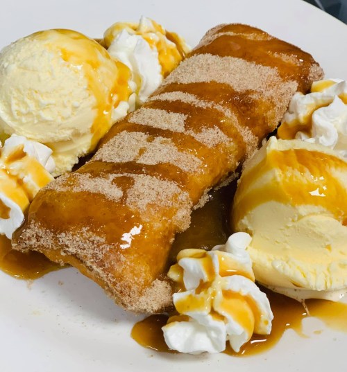 A dessert plate featuring a cinnamon-sugar rolled pastry with ice cream, whipped cream, and caramel sauce.