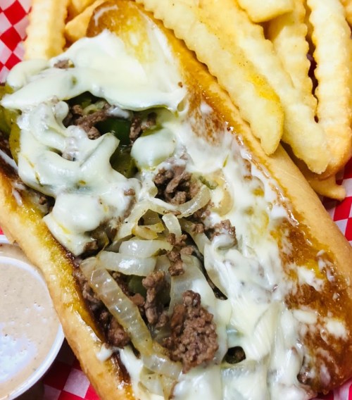 A cheesy beef sandwich with onions and peppers, served with crinkle-cut fries and a dipping sauce on the side.