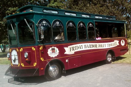 A colorful trolley bus with "Friday Harbor Jolly Trolley" signage parked in a green area.