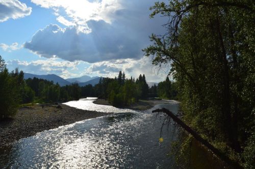A winding river flows through a lush landscape, with mountains and clouds in the background under a bright sky.