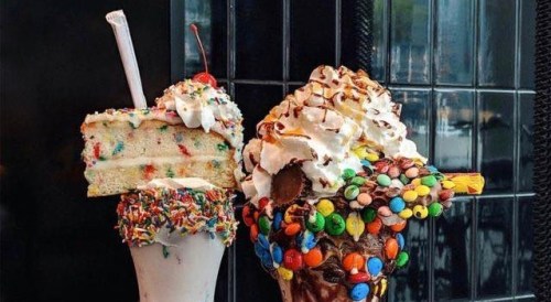 Two extravagant desserts: a colorful milkshake topped with cake and a candy-covered ice cream cone with whipped cream.