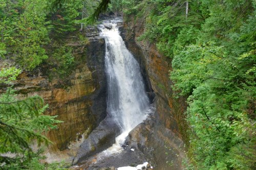 A cascading waterfall flows down a rocky cliff, surrounded by lush green trees and foliage.