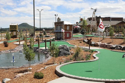A scenic mini-golf course with green turf, water features, and themed structures under a blue sky.