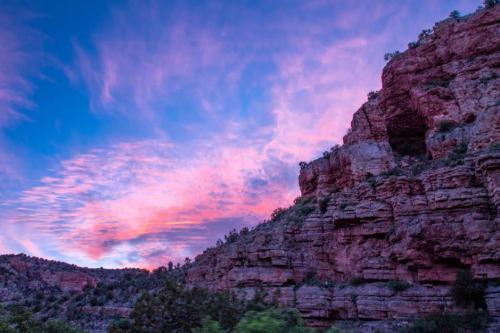 A vibrant sunset paints the sky in pink and purple hues above rugged rock formations and greenery.