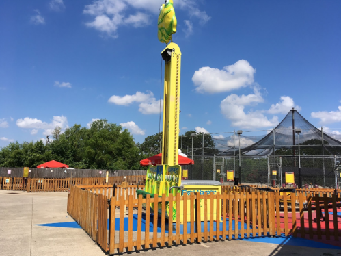 A colorful amusement park attraction featuring a giant hand, surrounded by wooden fencing and blue flooring under a clear sky.
