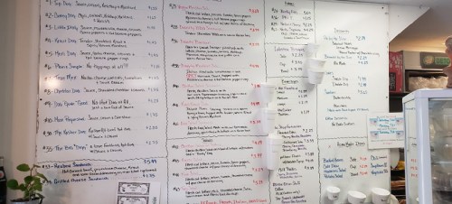 Menu board featuring various food and drink items with prices, written in black on a white wall.