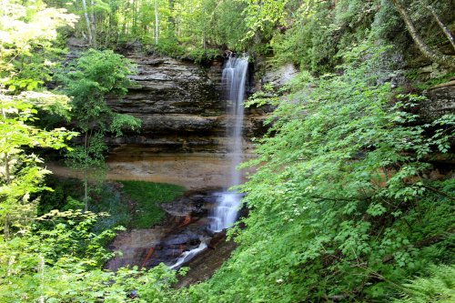 A serene waterfall cascading down rocky cliffs, surrounded by lush green foliage and trees.