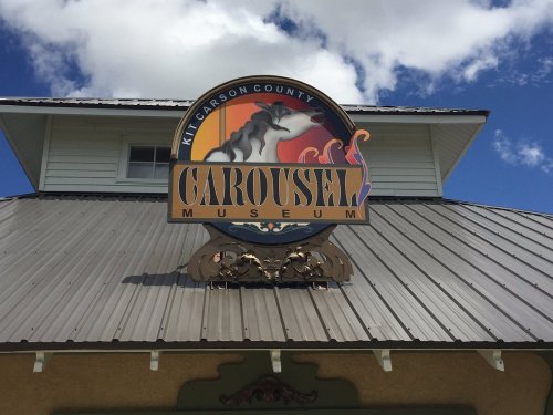 Sign for the Kit Carson County Carousel Museum, featuring a horse and colorful design against a blue sky.