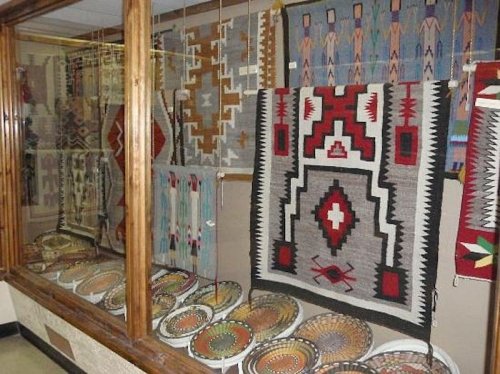 Display of colorful woven textiles and pottery in a glass case, showcasing intricate patterns and designs.