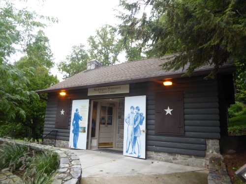 Log cabin-style building with a sign reading "Washington Monument Visitors Center" and blue illustrations on the doors.