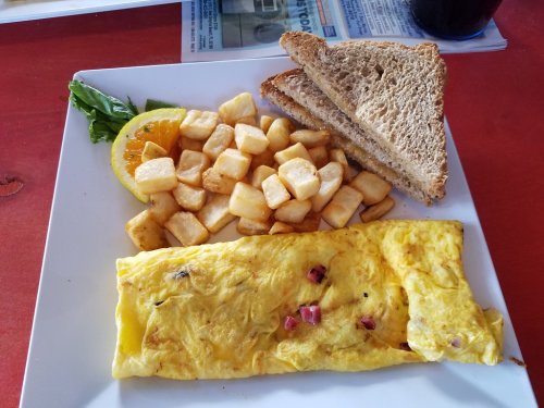 A plate with a fluffy omelette, diced potatoes, toast, and a slice of orange, garnished with a leafy green.