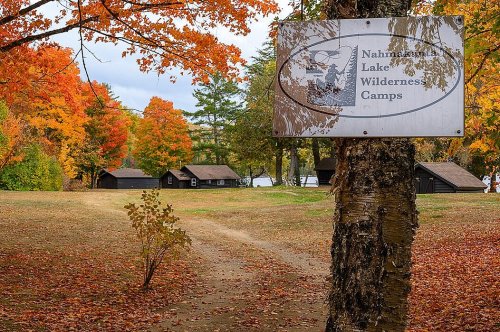 Sign for Nahmakanta Lake Wilderness Camps surrounded by vibrant autumn foliage and rustic cabins.