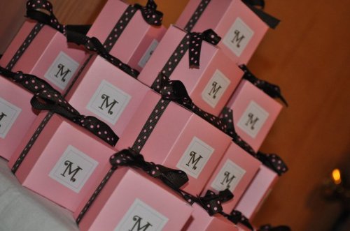 A stack of pink gift boxes tied with black polka dot ribbons, each featuring a white label with the letter "M."