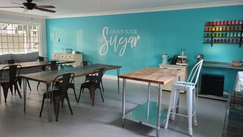 Bright turquoise room with wooden tables, chairs, and a wall sign that says "Gimme Some Sugar." Cozy and inviting atmosphere.