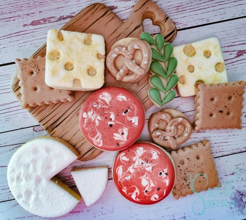 A variety of decorated cookies on a wooden board, including shapes like squares, circles, and pretzels in vibrant colors.