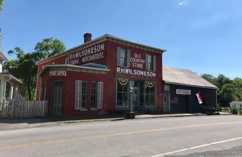 Historic red building with "R.H. Wilson & Son" signage, featuring a post office and antique shop, set on a sunny street.