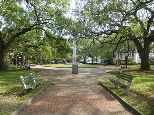 A peaceful park scene with benches, a stone monument, and lush green trees creating a serene atmosphere.