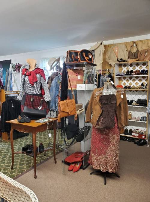 A vintage clothing store display featuring various outfits, accessories, and shoes on racks and mannequins.