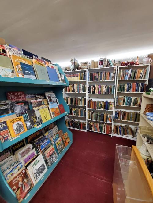 A cozy bookstore aisle with colorful shelves filled with books and magazines, surrounded by more bookshelves in the background.