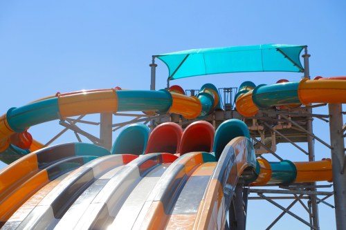 Colorful water slides with a blue sky in the background, featuring a shaded platform at the top.