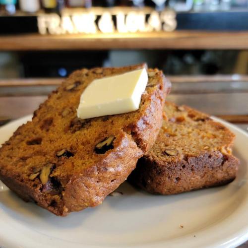 Two slices of pumpkin bread topped with a pat of butter on a white plate, with a blurred background.