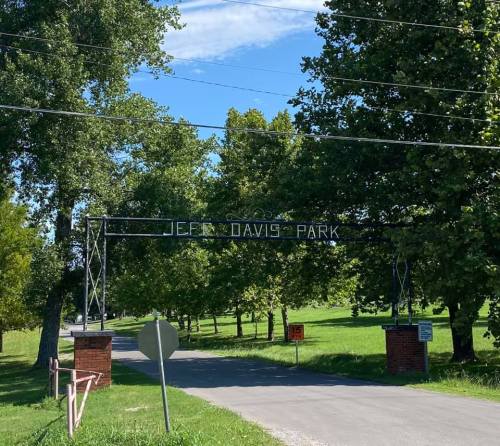 Entrance to Jeff Davis Park, featuring a metal archway and lush green trees under a clear blue sky.