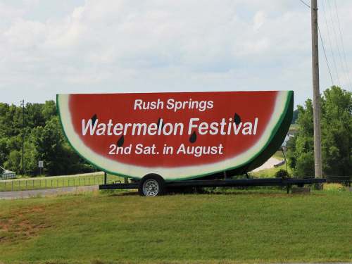 A large billboard advertising the Rush Springs Watermelon Festival, scheduled for the second Saturday in August.
