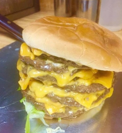 A towering cheeseburger with three beef patties, melted cheese, and lettuce, all sandwiched in a soft bun.