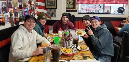 A group of five friends enjoying burgers and fries at a diner, smiling and having a good time together.