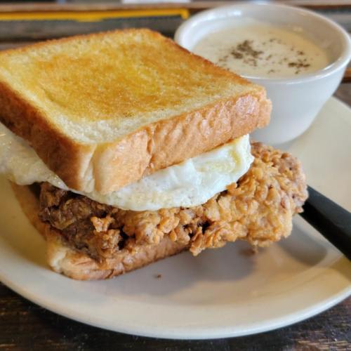 A plate featuring a fried chicken sandwich with a fried egg and toast, alongside a small bowl of creamy soup.