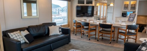 A modern living space with a black sofa, dining area, and large windows overlooking a marina.