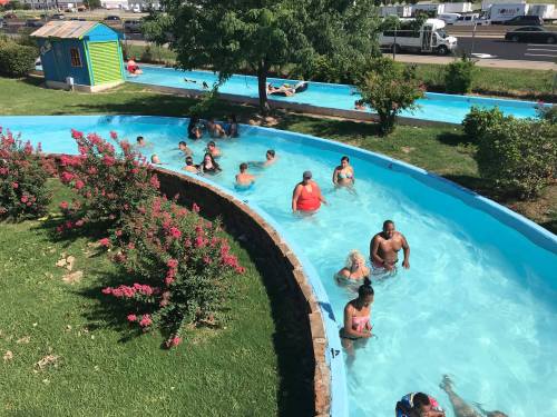 A water park scene with people enjoying a lazy river, surrounded by greenery and colorful structures.