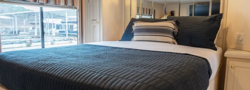 Cozy bedroom with a neatly made bed, blue quilt, and large window overlooking a marina.