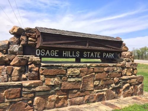 Sign for Osage Hills State Park, made of stone, with a blue sky and green grass in the background.