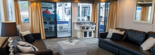 Cozy living area with black sofas, a coffee table, and large windows overlooking a boat dock.