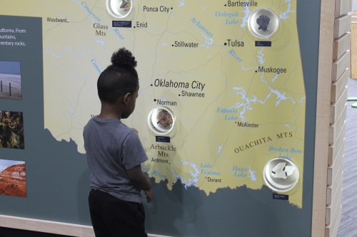 A child examines a map of Oklahoma with interactive displays highlighting various locations and features.