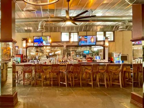 A spacious bar with wooden stools, multiple TVs, and a well-stocked counter in a modern setting.