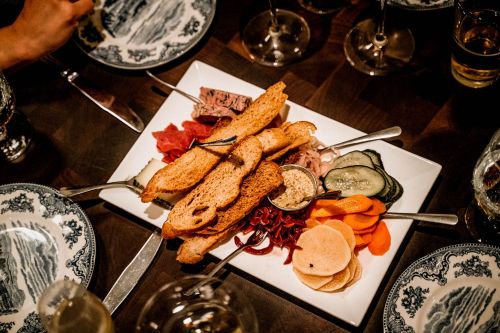 A platter of assorted meats, cheeses, pickles, and crackers, elegantly arranged on a white plate.