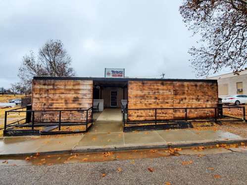 A wooden exterior building with a sign, surrounded by wet pavement and fallen leaves on a cloudy day.