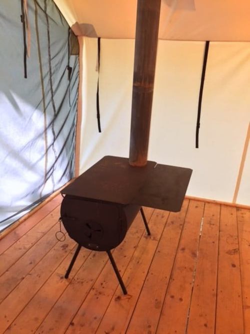 A black wood stove with a chimney inside a tent, resting on a wooden floor.