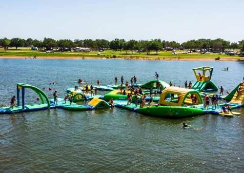 A vibrant inflatable water park with people playing and swimming in a lake on a sunny day.