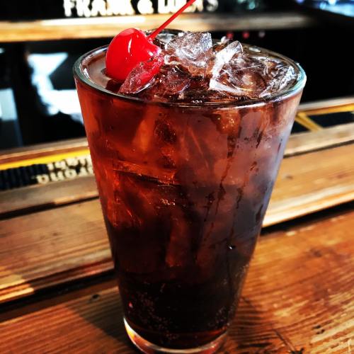A tall glass filled with ice and a dark beverage, topped with a cherry.